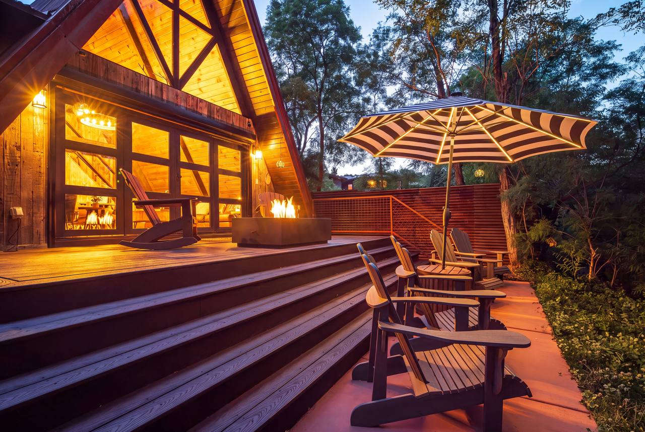 Deck with fire pit, Adirondack chairs, and green trees — summer