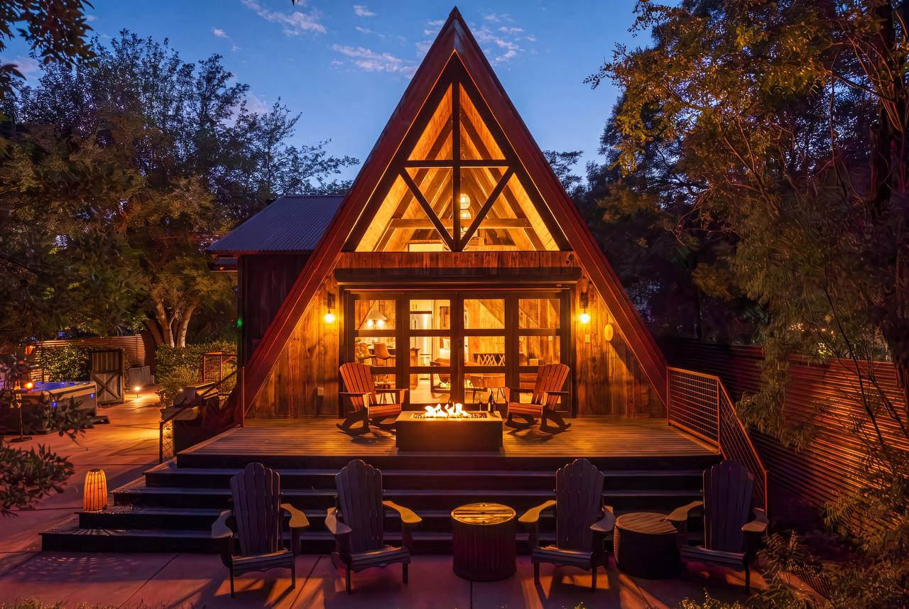 Front of A-frame at twilight with fire pit and green trees — summer
