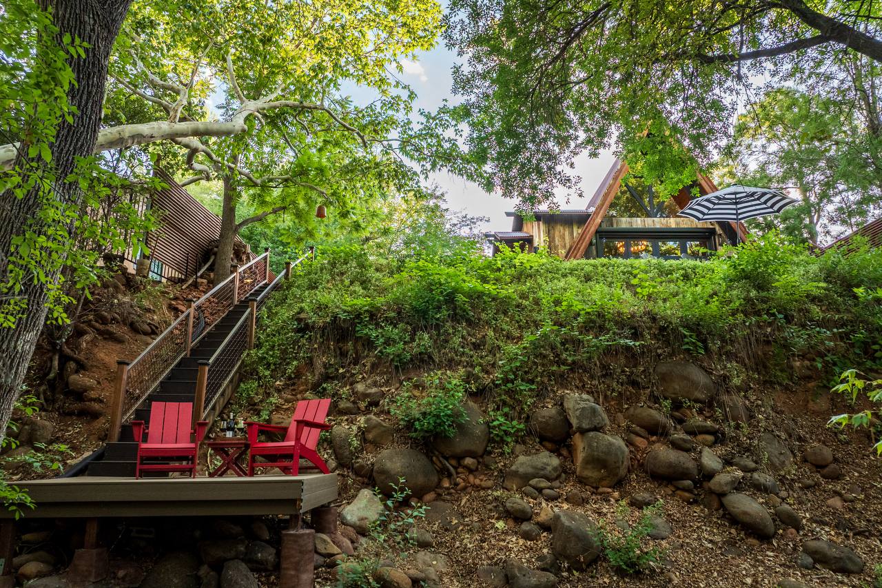 Back of Creekside 88 A-frame with stairs down to private creek deck with red chairs — summer greenery
