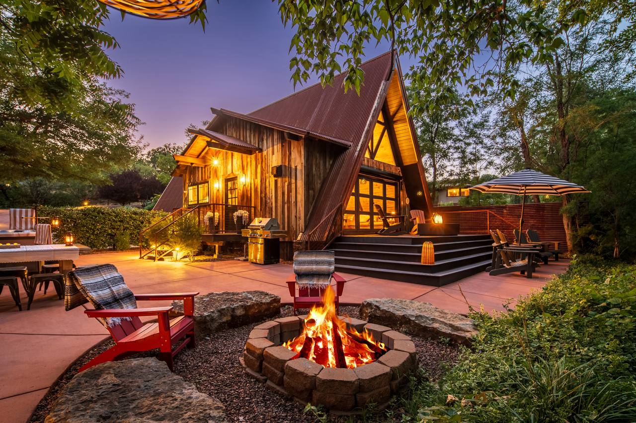 Wide shot of A-frame with stone fire pit and red chairs — summer