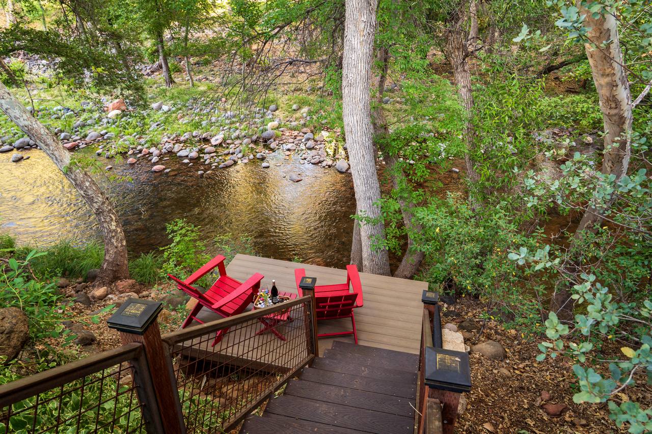 Looking down stairs to creek deck with red chairs and wine — summer