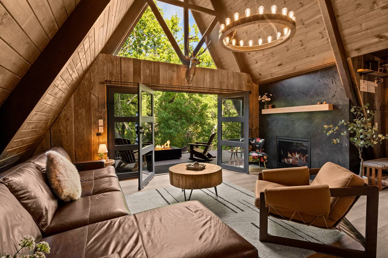 Living room with leather sectional, iron chandelier, and green trees through doors — summer